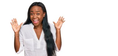 Genç siyah kadın gündelik giysiler giyip çılgınlığı kutluyor ve başarı için hayrete düşüyor kollarını kaldırıyor ve gözleri açık heyecanla bağırıyor. Kazanan konsept 