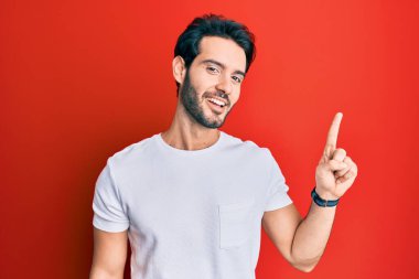 Gündelik beyaz tişört giyen genç İspanyol adam başarılı bir fikri işaret ediyor. Heyecanlı ve mutlu. Bir numara.. 