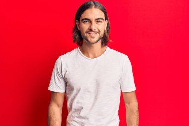 Yüzünde mutlu ve havalı bir gülümseme olan sıradan kıyafetler giyen genç yakışıklı bir adam. şanslı kişi. 