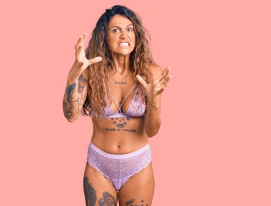 Dövmeli, iç çamaşırlı genç bir kadın öfkeyle bağırıyor, elleri boğmaya çalışıyor, deli gibi bağırıyor. 