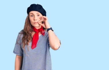 Fransız beresi takan, çizgili tişört giyen, dudaklarını parmaklarıyla kapatan genç ve güzel bir sarışın kadın. gizli ve sessiz, tabu konuşması 