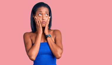 Genç Afro-Amerikalı kadın günlük yaz kıyafetleri giyiyor. Yorgun eller yüzünü kapatıyor, depresyon ve üzüntü yaşıyor. Sorunlardan rahatsız ve rahatsız. 