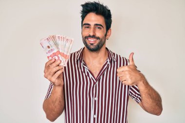 Kolombiya pezosu sakallı yakışıklı, mutlu ve pozitif gülümseyen, başparmağıyla mükemmel ve onay işareti yapan bir adam. 