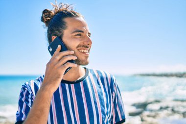 Genç İspanyol gülümseyen adam sahilde akıllı telefondan konuşarak mutlu oluyor..