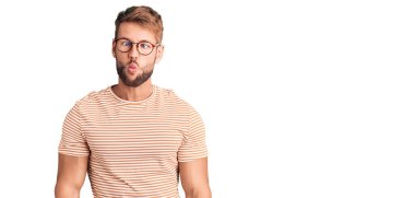 Günlük kıyafetler ve gözlük takan genç beyaz bir adam dudaklarıyla balık suratı yapıyor, çılgınca ve komik bir jest. Komik ifade. 