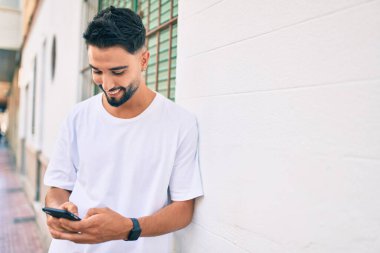 Genç Arap adam şehirde akıllı telefon kullanarak mutlu gülümsüyor..