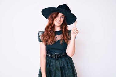 Cadı cadılar bayramı kostümü giymiş genç ve güzel bir kadın başarılı bir fikri işaret ediyor. Heyecanlı ve mutlu. Bir numara.. 