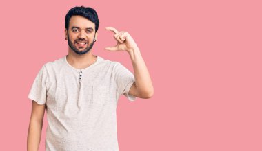 Gündelik kıyafetler giyen, gülümseyen, kendine güvenen, el hareketi yapan, parmaklarıyla işaret yapan ve kameraya bakan genç İspanyol bir adam. ölçüm kavramı. 