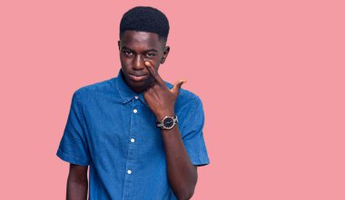 Gündelik giysiler giymiş genç Afro-Amerikan bir adam senin jestini izlerken, şüpheli bir ifade takınıyor. 