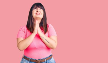 Genç ve cüsseli bir kadın gündelik giysiler giyip elleri bağlı yalvarıyor ve dua ediyor. Yüzünde umut ifadesi var. Çok duygusal ve endişeli. Yalvarıyor. 