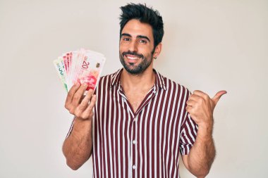 Sakallı yakışıklı İspanyol bir adam İsrail şekeri tutuyor başparmağını yana kaldırıyor ve ağzı açık gülümsüyor. 