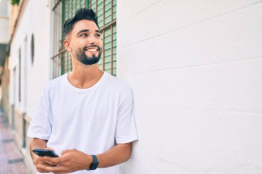 Genç Arap adam şehirde akıllı telefon kullanarak mutlu gülümsüyor..