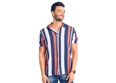 Yazlık tişört giyen genç yakışıklı İspanyol adam yüzünde gülümsemeyle yan yana bakıyor, doğal bir ifade. Kendinden emin gülen. 