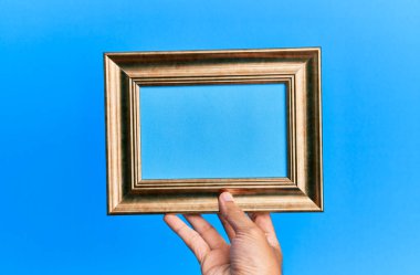 İzole edilmiş mavi arka planda eski bir çerçeveyi tutan İspanyol bir adamın eli..