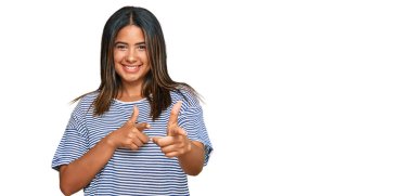 Gündelik kıyafetler giyen genç Latin kız mutlu ve komik yüzüyle kamerayı işaret ediyor. iyi enerji ve titreşimler. 