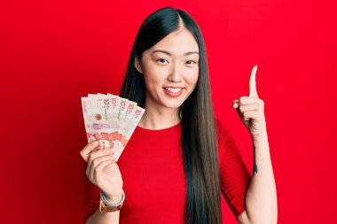 Elinde 10 Kolombiya pezosu olan genç Çinli bir kadın bir fikir veya soru işareti ile gülümsüyor. 