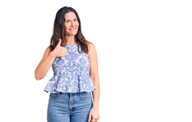 Genç, güzel, esmer, sıradan tişörtler giyen bir kadın mutlu bir el hareketi yapıyor. Kameraya bakıp başarıyı gösteren ifade. 