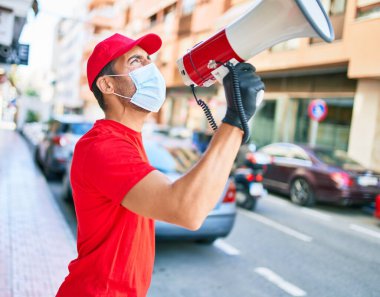Üniforma giyen ve koronavirüs koruma maskesi takan genç teslimatçı. Şehir sokağında megafonla bağırıyordu..