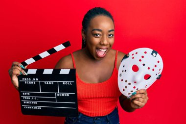 Genç Afro-Amerikalı kadın elinde video film panosu ve korku maskesi tutuyordu. Gülüşmeler ve kahkahalar atıyordu.. 