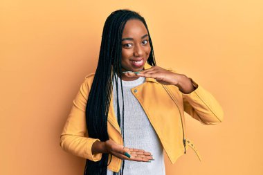 Genç Afro-Amerikalı kadın, sıradan bir ceket giyiyor. Elleri büyük ve büyük bir işaret gösteriyor. Ölçü sembolü. Kameraya bakıp gülümsüyor. ölçüm kavramı. 
