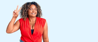 Genç Afro-Amerikan artı cüsseli kadın kolsuz tişörtlü rahat giyiniyor kameraya bakıp parmaklarını zafer işareti yaparken gösteriyor. İki numara.. 