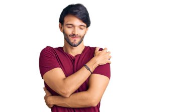 Yakışıklı, sıradan kıyafetler giyen, kendine sarılan mutlu ve pozitif, kendinden emin gülümseyen bir İspanyol. Sevgi ve özgüven. 