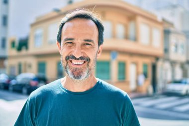 Orta yaşlı, sakallı, açık havada mutlu gülümseyen bir adam.