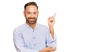 Yakışıklı, orta yaşlı, iş gömleği giyen, yüzünde kocaman bir gülümseme olan, eli ve parmağı kameraya bakan bir adam.. 