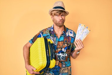 Yazlık kabin çantası tutan genç sarışın adam şüpheci ve gergin, sorun yüzünden surat asıyor. negatif kişi. 