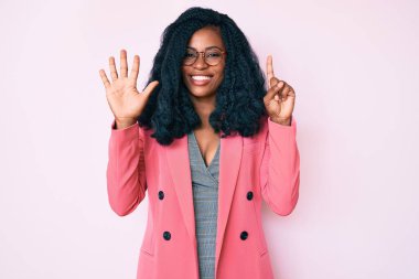 İş ceketi ve gözlük takan güzel Afrikalı kadın altı numaralı parmaklarını gösterip işaret ederken kendinden emin ve mutlu gülümsüyor.. 