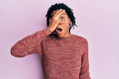 Sıradan bir kazak giyen genç Afro-Amerikalı adam şok içinde yüzünü ve gözlerini eliyle kapatıyor, parmaklarından korkuyla bakıyor. 