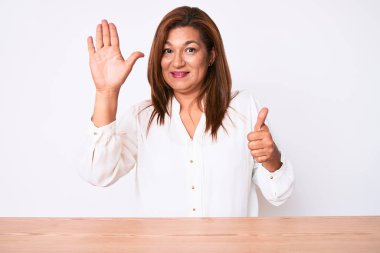 Orta yaşlı esmer, İspanyol iş kadını, gündelik beyaz gömlekli, masanın üzerinde oturuyor ve 6 numarayı işaret ediyor, kendinden emin ve mutlu bir şekilde gülümsüyor.. 