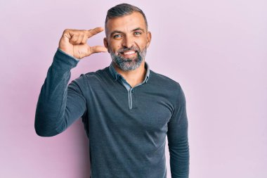 Orta yaşlı, sıradan kıyafetler giyen, gülümseyen, kendine güvenen, el hareketleriyle hareket eden, parmaklarıyla işaret yapan ve kameraya bakan yakışıklı bir adam. ölçüm kavramı. 