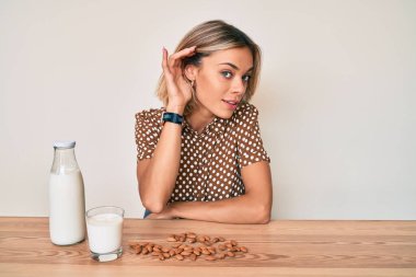 Sağlıklı badem sütü içen, ağzı kulaklarında gülümseyen, dedikoduları ve dedikoduları dinleyen beyaz bir kadın. Sağırlık kavramı. 