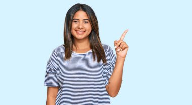 Gündelik kıyafetler giyen genç Latin kız bir numarayı gösterip işaret ederken kendine güvenen ve mutlu bir şekilde gülümsüyor.. 