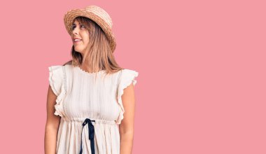 Yazlık şapka ve tişört giyen genç ve güzel bir kadın yüzünde gülümseme ve doğal bir ifadeyle yan yana bakıyor. Kendinden emin gülen. 