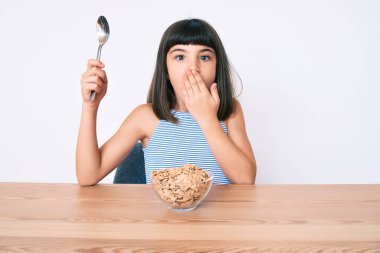 Bangır bangır küçük bir kız masada oturmuş gevrek yiyor ağızlarını eliyle kapatıyor, şok geçiriyor ve hata yapmaktan korkuyor. şaşırmış ifade 
