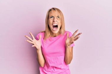 Sıradan pembe tişörtler giyen güzel sarışın kadın başarı için deli ve çılgınlığı kutluyor kolları havada ve gözleri kapalı heyecanla bağırıyor. Kazanan konsept 