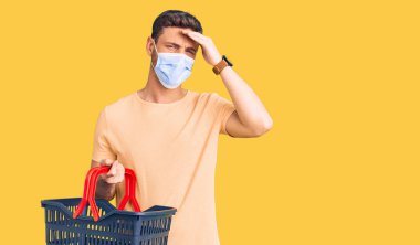 Alış veriş sepeti ve tıbbi maske takan yakışıklı genç bir adam. Elleri havada, şaşırmış ve sinirli bir yüzü var. 