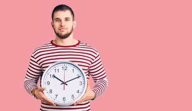 Büyük bir saat tutan yakışıklı genç adam. Düşünme tarzı ve ayık yüz ifadesi. Kendine güvenen biri. 