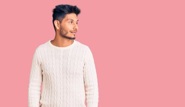 Yakışıklı Latin Amerikalı sıradan bir kazak giyen genç adam yüzünde gülümseme, doğal bir ifade ile yan yana bakıyor. Kendinden emin gülen. 