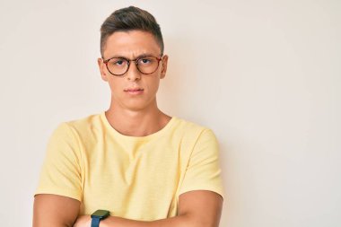 Gündelik kıyafetler giyen, gözlüklü, şüpheci ve gergin genç İspanyol çocuk. Yüzünde çapraz kollarla onaylamayan bir ifade var. negatif kişi. 