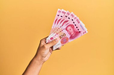 Çin malı 100 Yuan 'lık banknotları izole edilmiş sarı arka planda tutan İspanyol adamın eli..