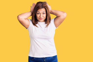 Orta yaşlı, beyaz tişört giyen, tavşan kulağı hareketi yapan, avuçlarıyla alaycı ve şüpheci görünen Latin bir kadın. Paskalya tavşanı konsepti. 