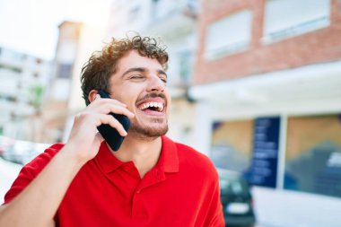 Genç yakışıklı beyaz adam mutlu gülümsüyor. Şehirdeki akıllı telefondan konuşuyorlar..