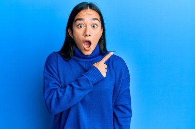 Kış süveteri giyen genç Asyalı kadın parmaklarını yana doğru göstererek şaşırdı, ağzı açık hayret içinde kaldı.. 