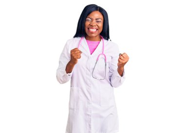 Doktor steteskobu giyen genç Afro-Amerikalı kadın kolları havada ve gözleri kapalı bir şekilde başarıyı kutluyor ve şaşırıyor. Kazanan konsept. 