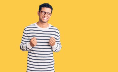 Gündelik kıyafetler ve gözlük takan İspanyol yakışıklı genç adam başarı için heyecanlanıyor kolları havada ve gözleri kapalı zaferi kutluyor. Kazanan konsept. 