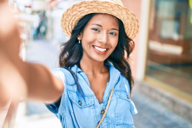 Genç, güzel, Hintli bir kadın. Yazlık şapka takıyor, gülümsüyor. Mutlu bir şekilde selfie çekiyor..