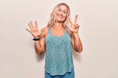 Orta yaşlı beyaz kadın spor giysisi giyer ve 8 numaralı parmaklarıyla işaret ederken kendinden emin ve mutlu gülümserdi.. 